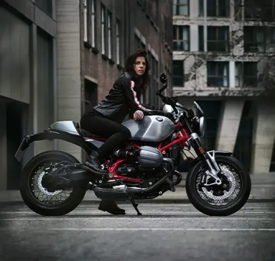 Static right side image of BMW Motorrad R 12 nineT Option 719 in Aluminium colourway, with female rider sitting on the motorcycle