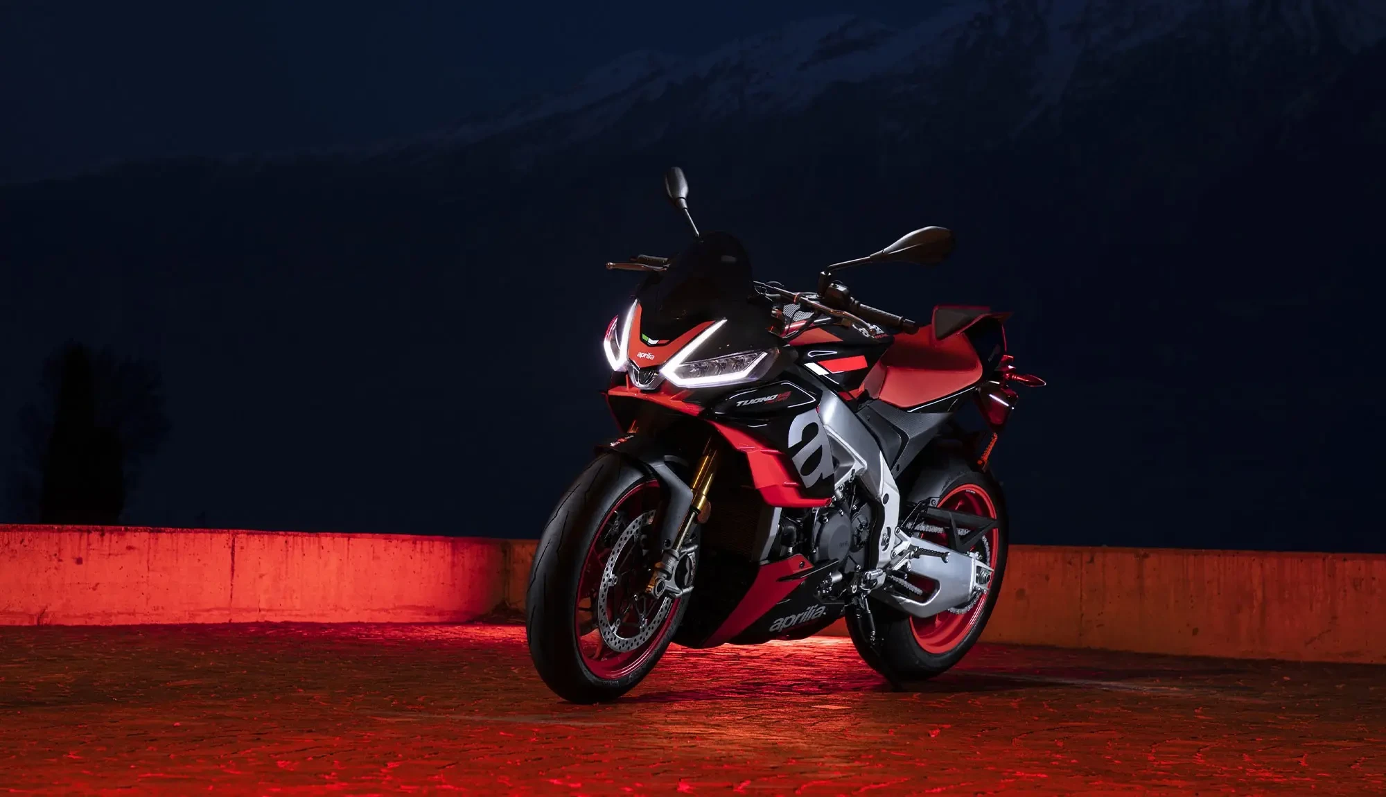 Front three quarter image of Aprilia Tuono Factory taken at night with red neon back light