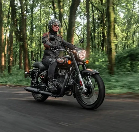 Action image of Royal Enfield Bullet 350 in Black/Gold colourway, female riding through forest road