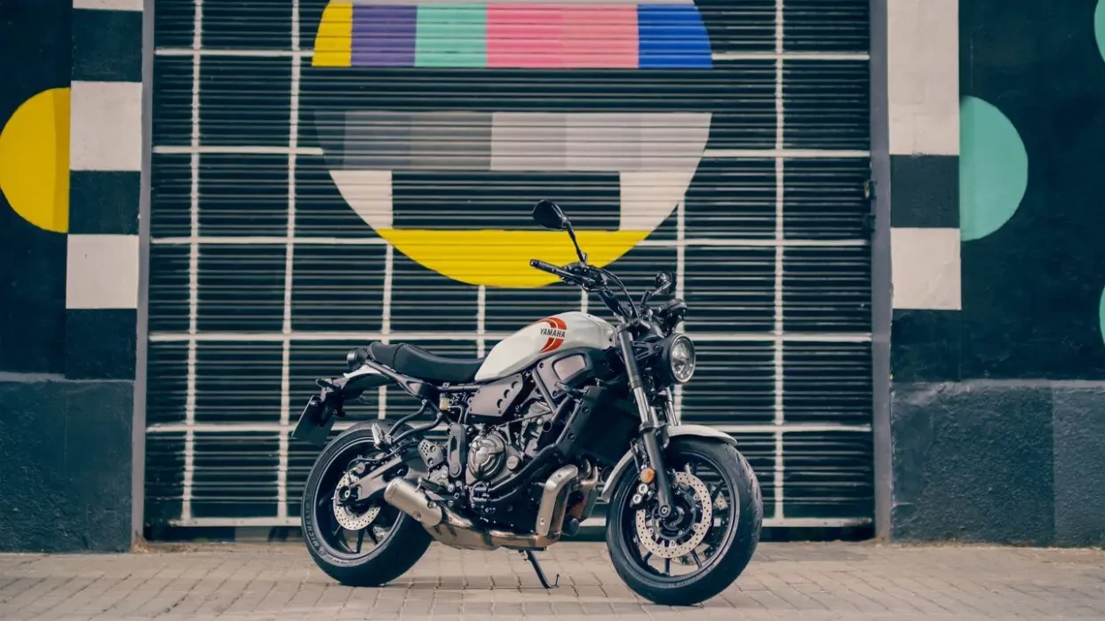 Static image of Yamaha XSR700 in white Colourway, front three quarter in front of funky test pattern painted garage door