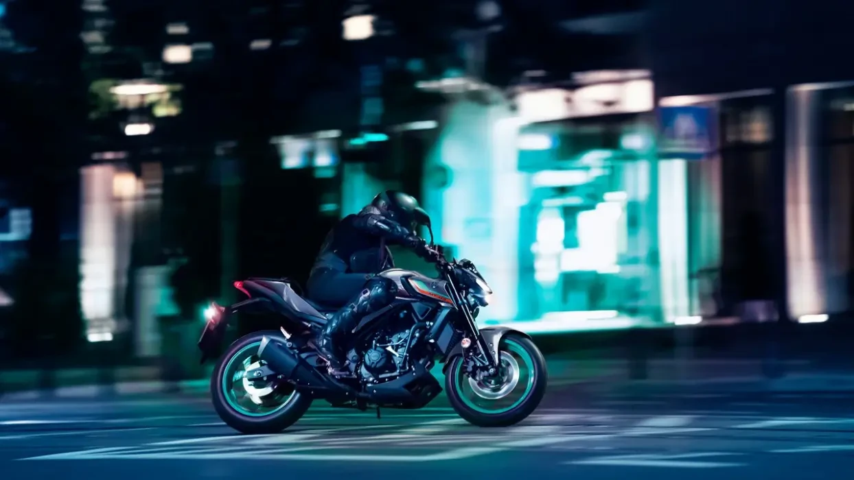 Action image of Yamaha MT-03 LAMS roadster in grey/aqua colourway, side on right, travelling through cityscape at night
