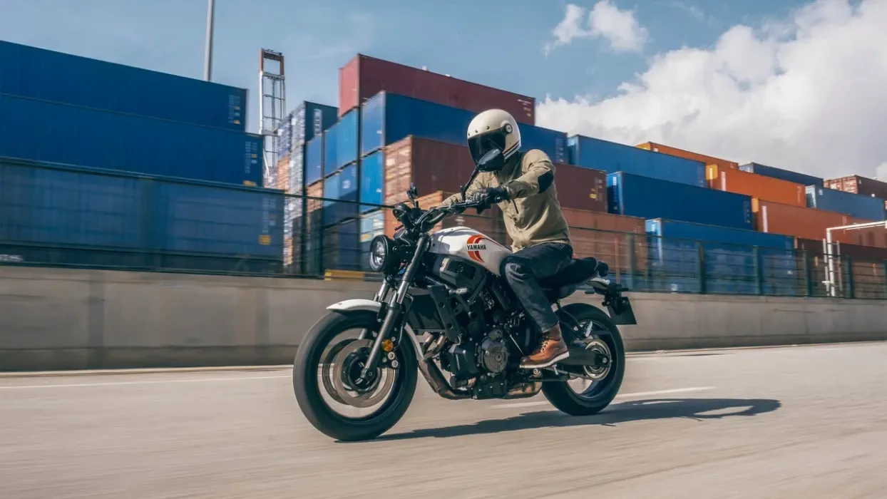 Action image of Yamaha XSR700 in white Colourway, tracking shot shipping containers in background