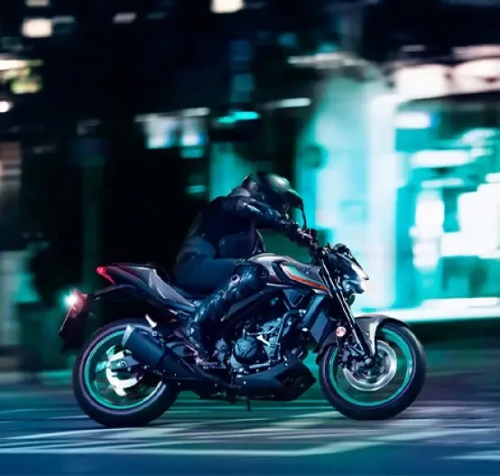 Action image of Yamaha MT-03 LAMS roadster in grey/aqua colourway, side on right, travelling through cityscape at night