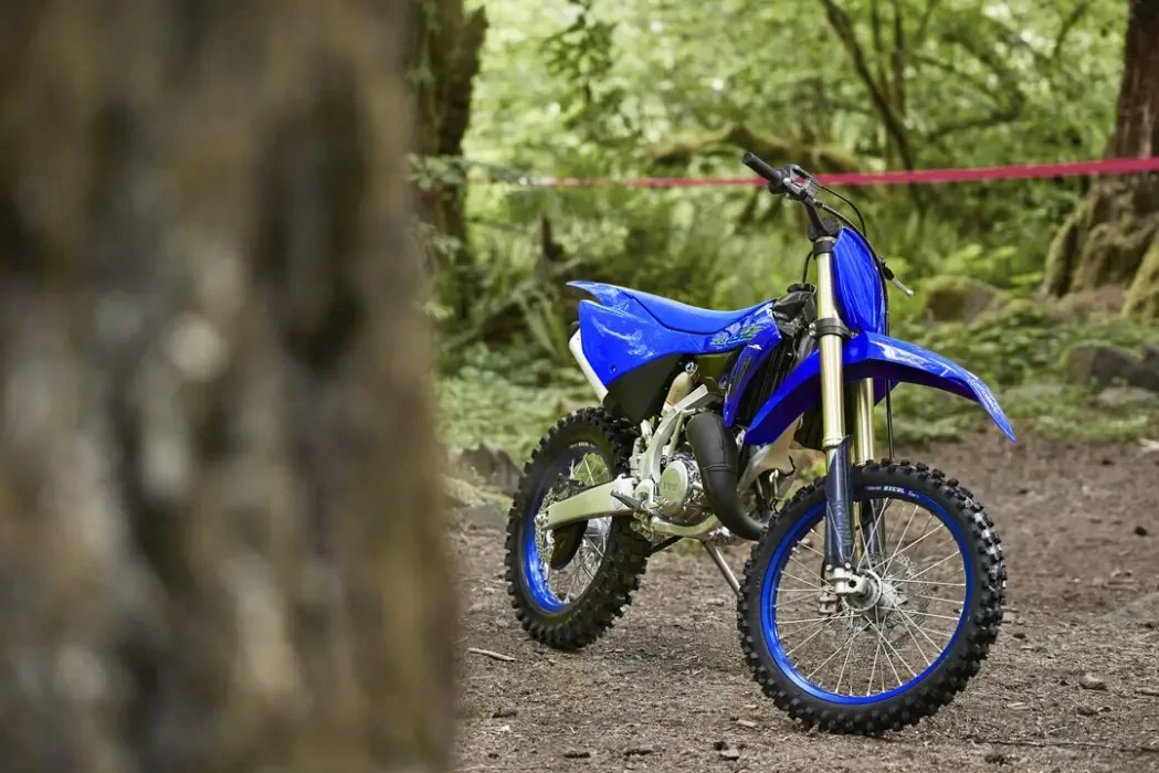 static image of Yamaha YZ125X two stroke in blue colourway, bike parked on forest trail