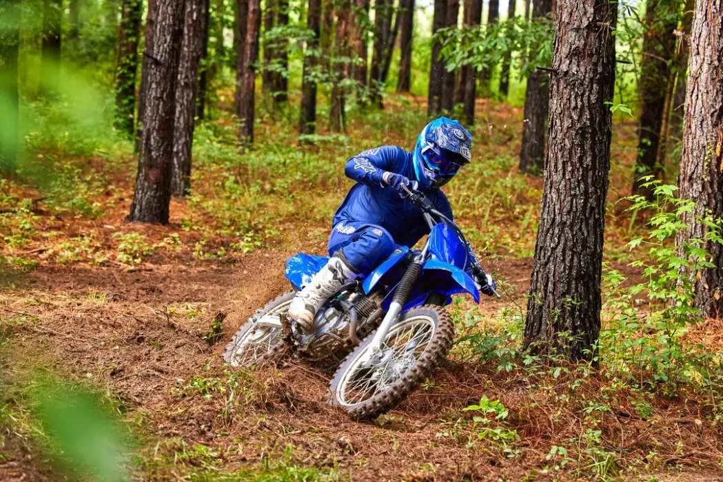 Action image of Yamaha TT-R230 2023 in Blue colourway, turning left in forest landscape