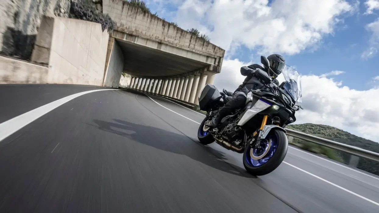 Action image of Yamaha Tracer 900 GT+, in Icon colourway, riding out of pilon tunnel